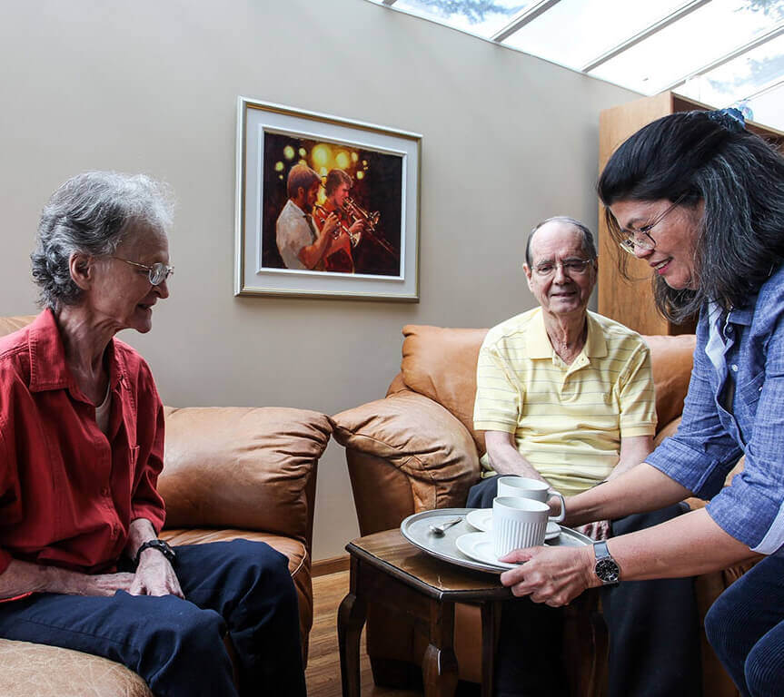 Home health Care professional serving tea to a senior couple